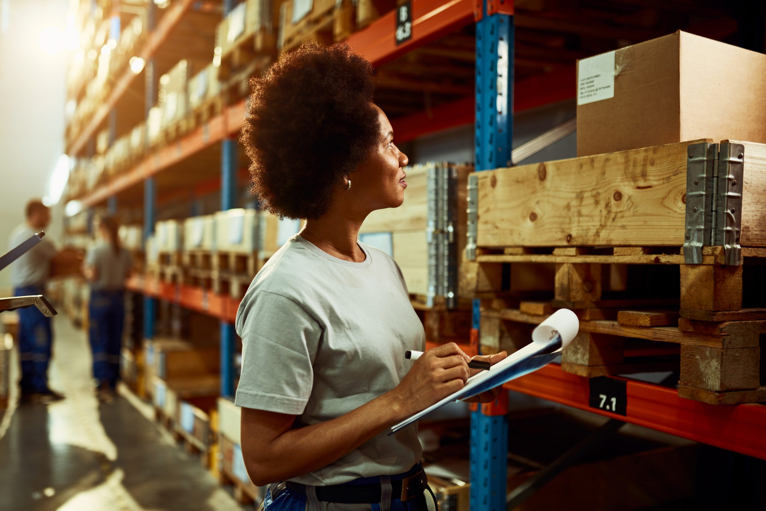 Black female warehouse worker taking notes while checking stock